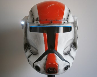 May include: A white and red helmet with a blue visor and a black stripe down the center. The helmet has a weathered look and is made of plastic.