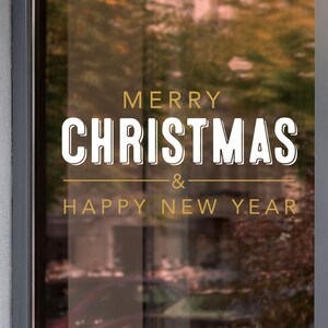 Può includere: Una finestra con un cartello dorato e bianco che dice "Buon Natale & Felice Anno Nuovo".