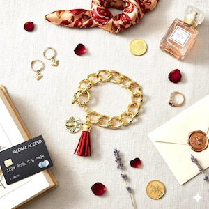 May include: A gold-toned chain bracelet with a red tassel and bee charm, paired with matching earrings. The image also features a floral scarf, perfume, coins, a ring, and a credit card.