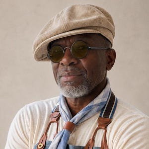 May include: A beige flat cap, round sunglasses, a light blue and white plaid neckerchief, a long-sleeved cream shirt, and a blue pinstriped apron with leather straps. The apron features the text REPEAL, EST 2011, MOTO, RIPE, and CLUP.