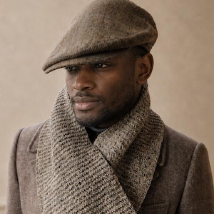 May include: A brown flat cap, a textured brown knit scarf, and a brown wool coat. The flat cap features a classic rounded shape with a short brim. The scarf has a thick, ribbed knit pattern in a heathered brown tone, and the coat is a solid brown.