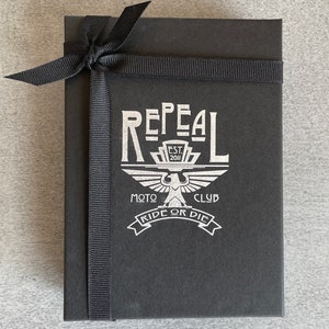 Repeal Moto Club Gremlin Bell Keychain in black leather and steel, featuring a winged wheel motif. A
perfect gift for motorcycle lovers and enthusiasts