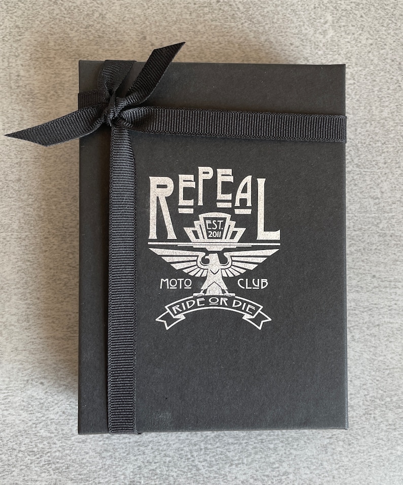 Repeal Moto Club Gremlin Bell Keychain in black leather and steel, featuring a winged wheel motif. A
perfect gift for motorcycle lovers and enthusiasts