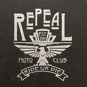 Repeal Moto Club Gremlin Bell Keychain in black leather and steel, featuring a winged wheel motif. A
perfect gift for motorcycle lovers and enthusiasts