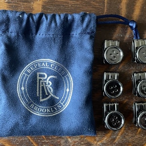 May include: Six black metal button clips with a blue velvet pouch. The pouch has the text "Repeal Club Brooklyn" printed on it.