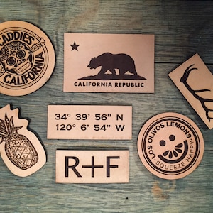 May include: Seven leather patches with various designs. One patch features a skull with the text "Mad Caddies Old California". Another patch features a bear with the text "California Republic". A third patch features a pineapple. A fourth patch features the text "34&deg; 39' 56" N 120&deg; 6' 54" W". A fifth patch features the text "R+F". A sixth patch features a deer antler. A seventh patch features a lemon with the text "Solivios Lemons, Squeeze Happy."