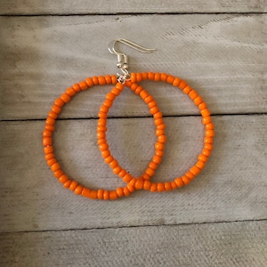 May include: A pair of orange beaded hoop earrings with silver hooks.