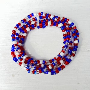 May include: Strands of beaded jewelry in red, white, and blue. The beads are small and round, and the strands are arranged in a circular pattern. The jewelry is likely worn around the waist or as a necklace.