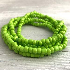 May include: A coiled bracelet made of small, round, lime green glass beads. The beads are uniform in size and shape, strung together to form a continuous loop that creates a layered, circular appearance with a bright, solid color finish.