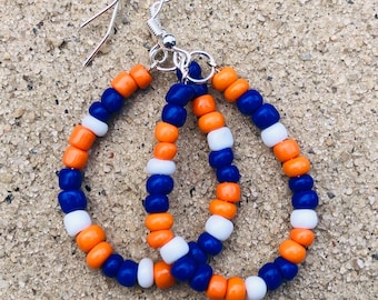 May include: A pair of teardrop-shaped earrings constructed from small, round beads in alternating colours of bright orange, deep blue, and white. The earrings feature silver-toned metal fishhook ear wires attached to the top of each beaded loop.