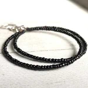 May include: A black beaded necklace with a silver clasp. The necklace is made of small, round beads and is layered twice.