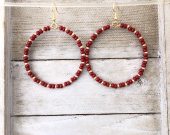 May include: A pair of hoop earrings featuring a circular design composed of alternating small red beads and tiny gold-toned metallic spacers. Each earring is suspended from a gold-toned metal fishhook style ear wire for secure attachment.