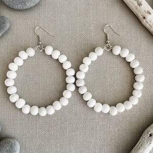 May include: A pair of hoop earrings constructed from a continuous circle of smooth, matte white spherical beads. Each earring features a silver-toned metal hook wire at the top, allowing the circular beaded structure to hang freely as a dangle earring.