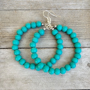 May include: A pair of hoop earrings constructed from circular turquoise-colored beads. The beads are strung together to form a continuous loop, connected at the top by silver-toned metal findings and standard earring hooks for attachment.