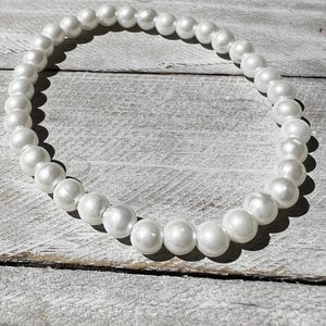 May include: A circular bracelet composed of numerous smooth, round, white faux pearls of uniform size. The beads are strung together in a continuous loop, reflecting light on their glossy surfaces, creating a simple and classic jewelry accessory.