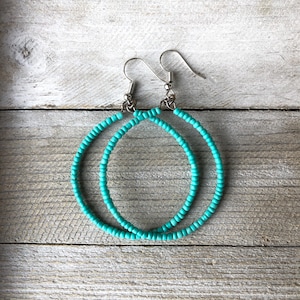 May include: A pair of hoop earrings constructed from small, round, turquoise-colored beads strung onto a circular wire frame. The earrings feature silver-toned metal fishhook-style ear wires for attachment, creating a simple, circular design.