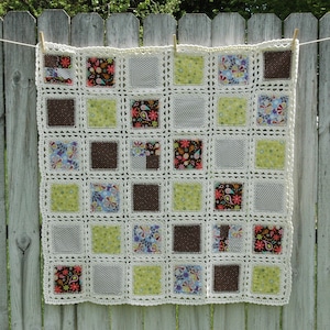 May include: A crocheted blanket with a white background and squares of different colored fabrics. The fabric squares feature various patterns, including paisley, floral, and polka dots.
