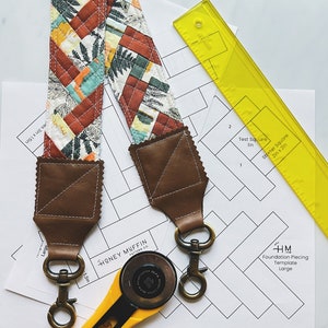 May include: Two brown leather straps with metal clasps, a yellow rotary cutter, and a printed paper template for foundation piecing. The template is labeled "HM Foundation Piecing Template Large".