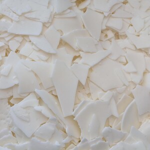 May include: A close-up of a pile of white wax flakes. The flakes are irregular in shape and size, and they are all very white.