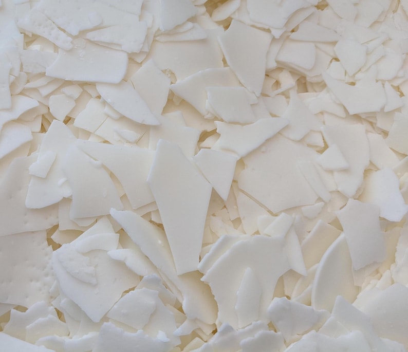 May include: A close-up of a pile of white wax flakes. The flakes are irregular in shape and size, and they are all very white.