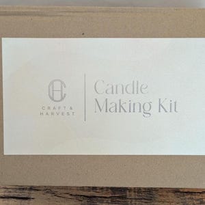 Pu&ograve; includere: Una scatola rettangolare di cartone marrone con un'etichetta bianca. L'etichetta presenta il testo "Candle Making Kit" e il logo "Craft & Harvest". La scatola &egrave; su una superficie di legno.