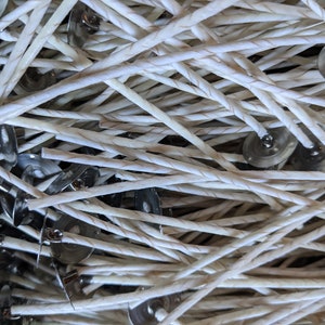 May include: Close-up of a pile of candle wicks with metal bases. The wicks are white, braided, and have a slight beige hue. The metal bases are silver and circular, designed to hold the wicks in place during candle making.