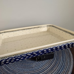 May include: Rectangular ceramic baking dish with a cream-colored interior and a blue and white patterned border. The dish has a dotted pattern inside and a decorative blue border with a scalloped design. A versatile kitchenware item.