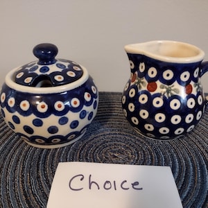May include: A ceramic sugar bowl with a lid and a small creamer. Both pieces are decorated with a blue and white pattern of dots and circles. The creamer has a handle and a spout. The sugar bowl has a small spoon opening.