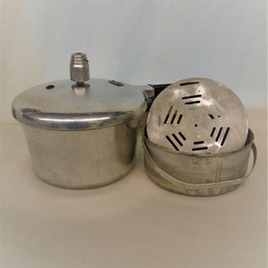 May include: A silver pressure cooker with a lid and a silver steamer insert with a handle. The steamer insert has a perforated bottom.