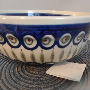 May include: A ceramic bowl with a white interior and a blue exterior band. The bowl features a decorative pattern of blue, green, and red accents. The bowl is approximately 7 inches in diameter and 2.75 inches tall.