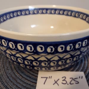 May include: A ceramic bowl with a cream-colored interior and a blue patterned exterior. The bowl has a 7-inch diameter and is 3.25 inches tall. The rim and exterior are decorated with a repeating blue design.
