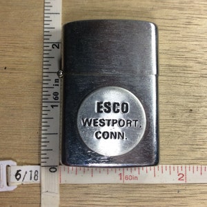 May include: Silver lighter with a round, embossed logo that reads "ESCO WESTPORT, CONN."