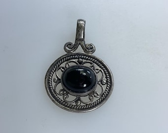 Pode incluir: Um pingente de prata com uma pedra preciosa preta engastada em um design filigranado.