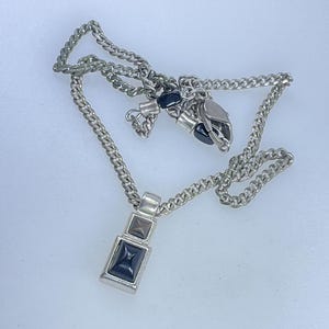 May include: A silver chain necklace with a black stone pendant. The pendant is rectangular and has a small, square black stone in the center.