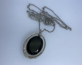 May include: A silver chain necklace with a pendant featuring a large black oval gemstone surrounded by a smaller circle of clear rhinestones.