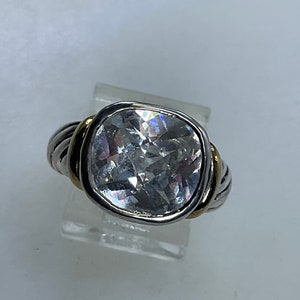 May include: A silver and gold ring with a large, clear, square-shaped gemstone.