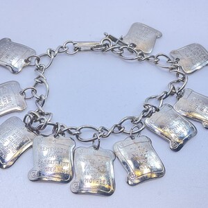 May include: Silver-toned charm bracelet featuring ten rectangular charms with engraved text. The charms are connected by a chain and clasp. The text on the charms is partially visible, with phrases like "Honor thy father and mother" and "Thou shalt not steal."