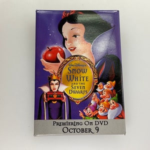 May include: A purple and silver DVD case featuring Snow White and the Seven Dwarfs. The case has a picture of Snow White holding a red apple and the Evil Queen holding a magic mirror. The text on the case reads "Walt Disney's Snow White and the Seven Dwarfs" and "Premiering on DVD October 9".