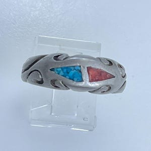 May include: A silver ring with a turquoise and coral inlay. The ring has a decorative design with swirls and curves.