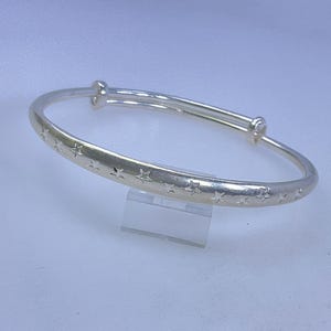 May include: A silver adjustable bangle bracelet with a star pattern. The bracelet is made of a shiny metal and has a simple, elegant design. The stars are evenly spaced around the bracelet.