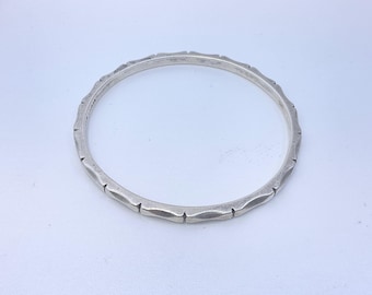May include: A circular silver bangle bracelet featuring a repeating pattern of small, evenly spaced notches along the outer edge. The metal has a smooth, polished finish with subtle indentations that create a segmented, textured appearance.
