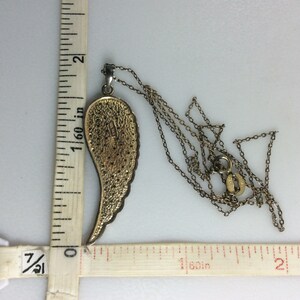 K&ouml;nnte beinhalten: Eine goldfarbene Engelsfl&uuml;gel-Anh&auml;ngerkette mit einer Kette, die etwa 3,8 cm lang ist. Der Anh&auml;nger ist etwa 3,8 cm lang und hat ein detailliertes Design.