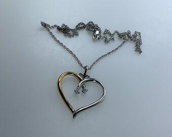 May include: A silver chain necklace with a two-toned heart pendant. The heart is made of silver and gold, and has three small diamonds in the center.