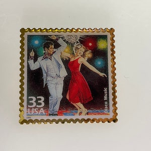 May include: A gold-framed 33 cent USA postage stamp featuring a couple dancing in a disco setting. The stamp is from 1999 and has the text "Disco Music" printed on the right side.