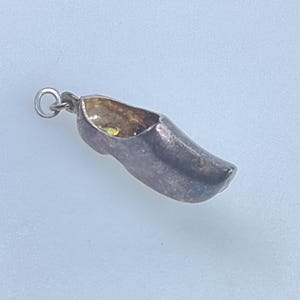 May include: Silver charm in the shape of a Dutch wooden shoe, or clog. The charm has a loop for attaching to a bracelet or necklace.