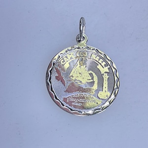May include: Silver-tone pendant with a detailed design. The round pendant features a textured border and a central image with the words "CAPE COD" and a lighthouse. A small clasp is attached at the top for hanging.