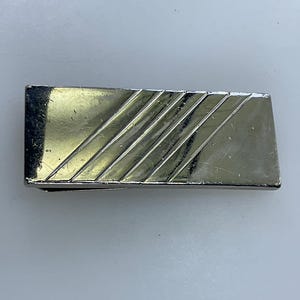 May include: A silver money clip with a diagonal line pattern.
