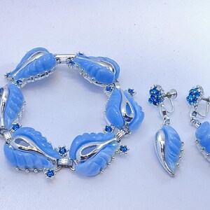 May include: A vintage jewelry set featuring a bracelet and clip-on earrings. The bracelet and earrings have a light blue tulip design with silver-tone metal accents and small blue crystal embellishments. The set is displayed on a white surface.