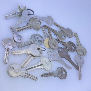 May include: A collection of various metal keys, some with key rings attached. The keys are in different shapes and sizes, with visible wear and tear, suggesting they are used. The keys are scattered on a light-colored surface.