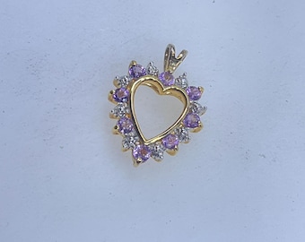 May include: A gold-toned heart-shaped pendant with a halo of small, round, purple gemstones and clear accent stones. The pendant has a simple bail for attaching to a chain. The heart shape is open in the center.